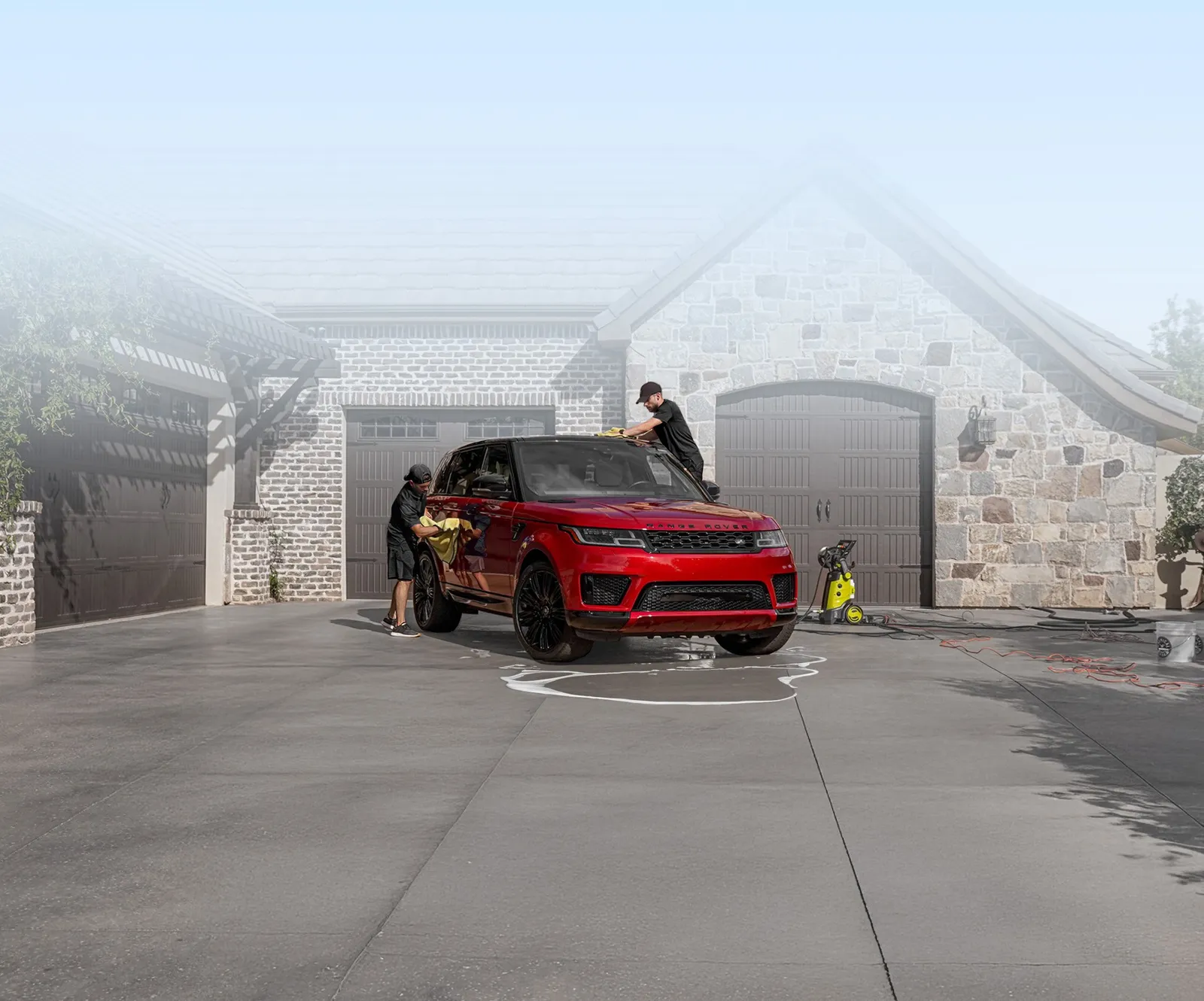 Two SudsCity crew members hand-drying a red SUV in the sun